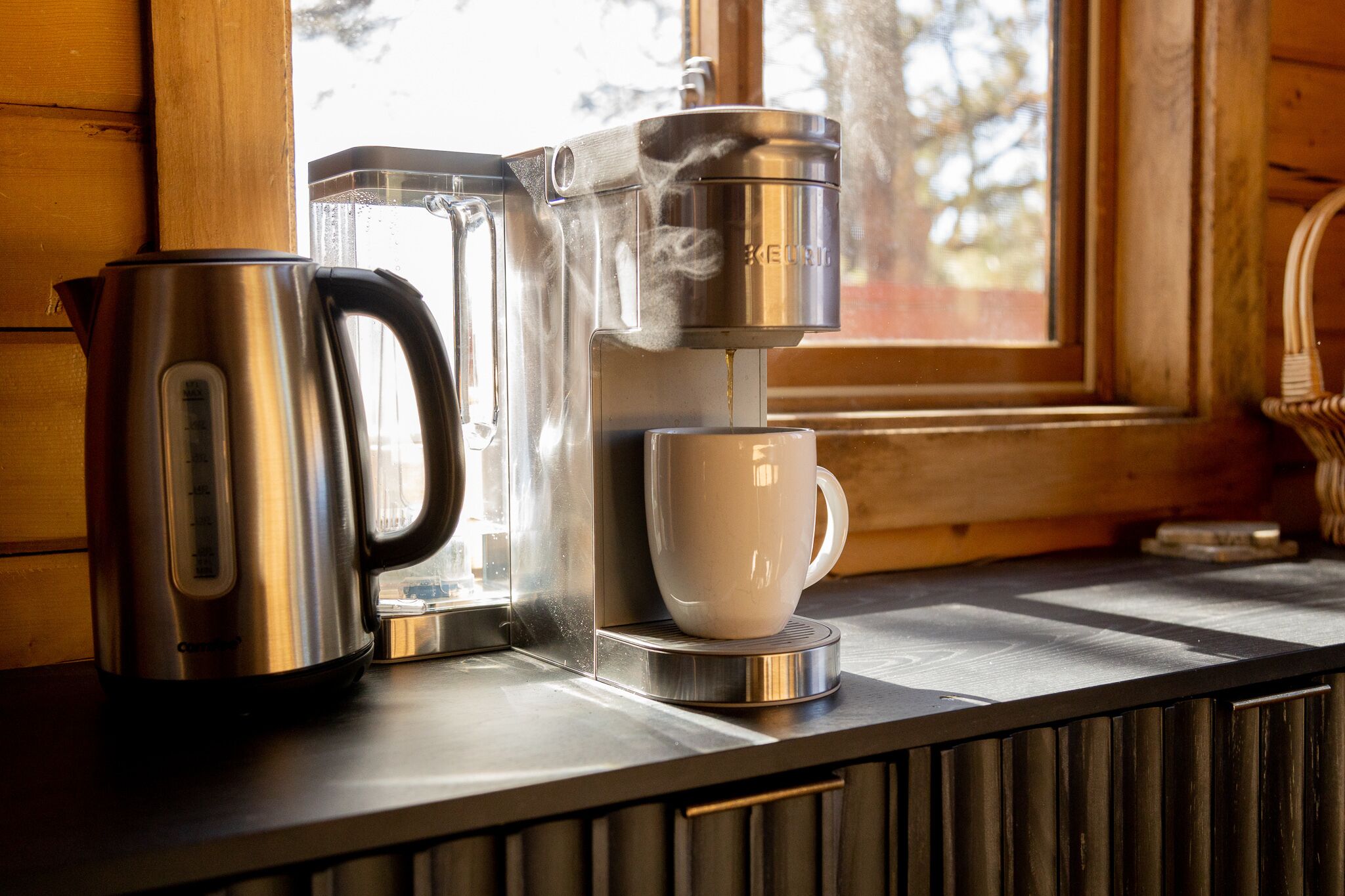 Eine Kaffeemaschine und eine Tasse auf einer Küchenarbeitsplatte in der Nähe eines Fensters.