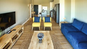 Un salon moderne avec un téléviseur à écran plat, une table basse en bois, des fauteuils jaunes et un canapé bleu.