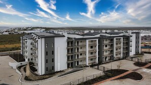 Un immeuble résidentiel moderne à plusieurs étages, doté de balcons, d’une cour aménagée et offrant une vue sur les environs.