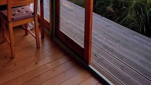 Une terrasse en bois avec une table et des chaises, offrant une vue sur un paysage et un coucher de soleil.