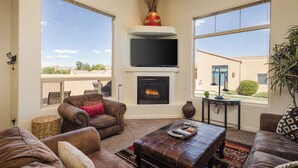 Un salón con sofás de cuero, chimenea, televisor de pantalla plana y ventanas amplias con vistas al paisaje.