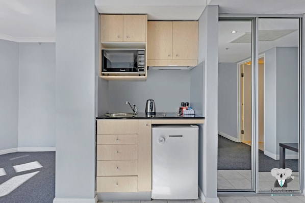 A compact kitchen with a microwave, kettle, and small refrigerator.
