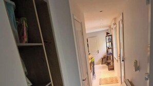 A narrow hallway with a built-in shelving unit on the left, a radiator on the right, and a door at the end leading to a room.