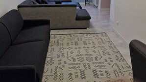 A modern living room with a sectional sofa, a patterned rug, and a flat-screen TV mounted on the wall.