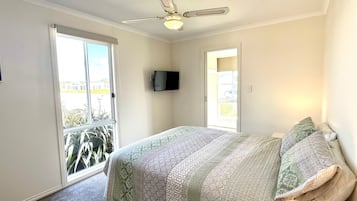 A bedroom with a bed, a ceiling fan, a TV, and a balcony door.