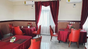 A restaurant with red tablecloths and matching chairs, air conditioning units on the wall, and a window with curtains. - Techiman (Techiman)