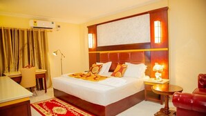 A hotel room with a large bed, a desk, a chair, a red armchair, and a small table with a lamp. - Techiman (Techiman)