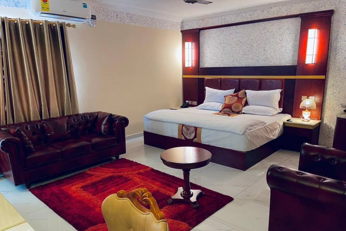 A hotel room with a large bed, a sofa, a small round table, and a chair.