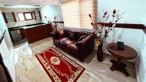 A living room with a red sofa, a coffee table, a vase with flowers, and a kitchen in the background. - Techiman (Techiman)