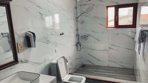 A bathroom with a marble wall, a toilet, a sink, and a shower. - Techiman (Techiman)