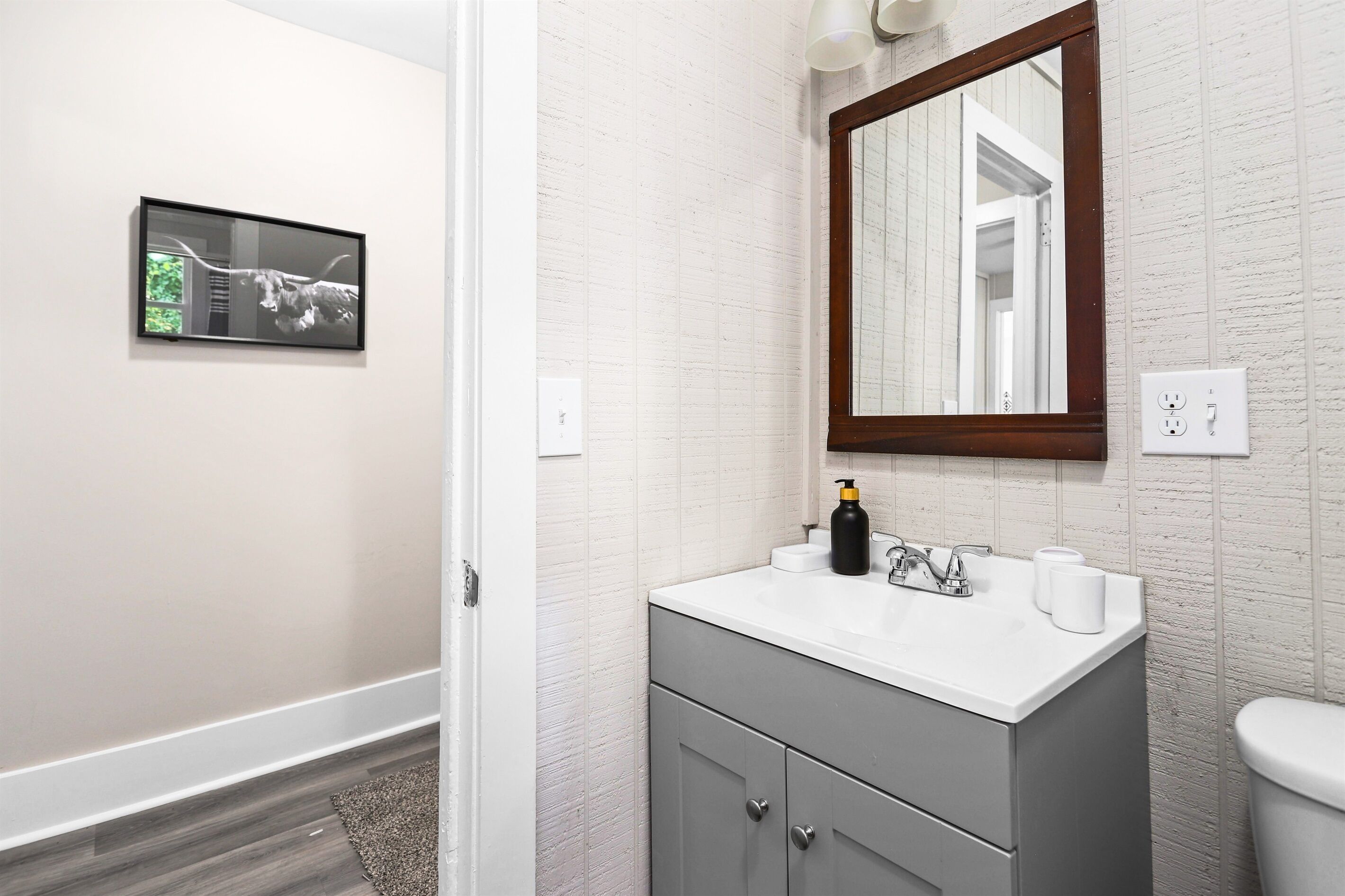 Une salle de bain avec un lavabo blanc, un miroir et un tableau encadré au mur.