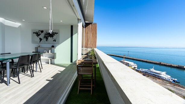 Um interior moderno com área de jantar, parede de destaque em madeira e vista para o mar e barcos.