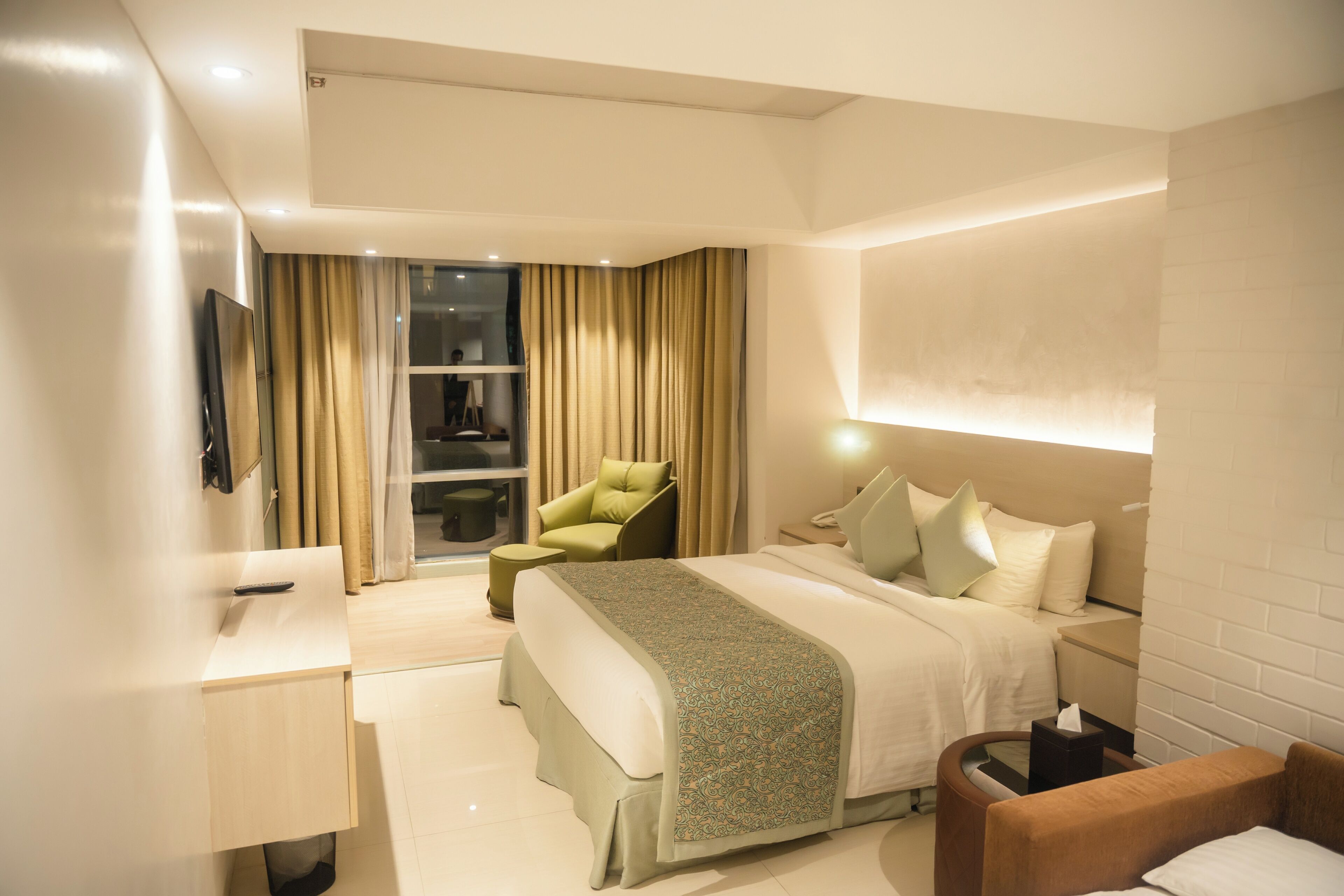 A hotel room with a bed, a desk, a chair, and a TV.