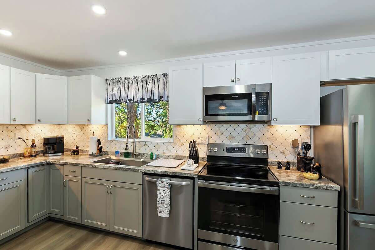 A modern kitchen with white cabinets, stainless steel appliances, and a window with a view of greenery.