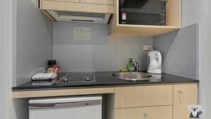 A compact kitchen with a dishwasher, a microwave, a sink, and a coffee maker. - KozyGuru | Sydney CBD | 2 Bed Studio (Haymarket)