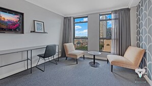 A hotel room with a large window, two armchairs, a small table, and a TV on the wall. - KozyGuru | Sydney CBD | 2 Bed Studio (Haymarket)