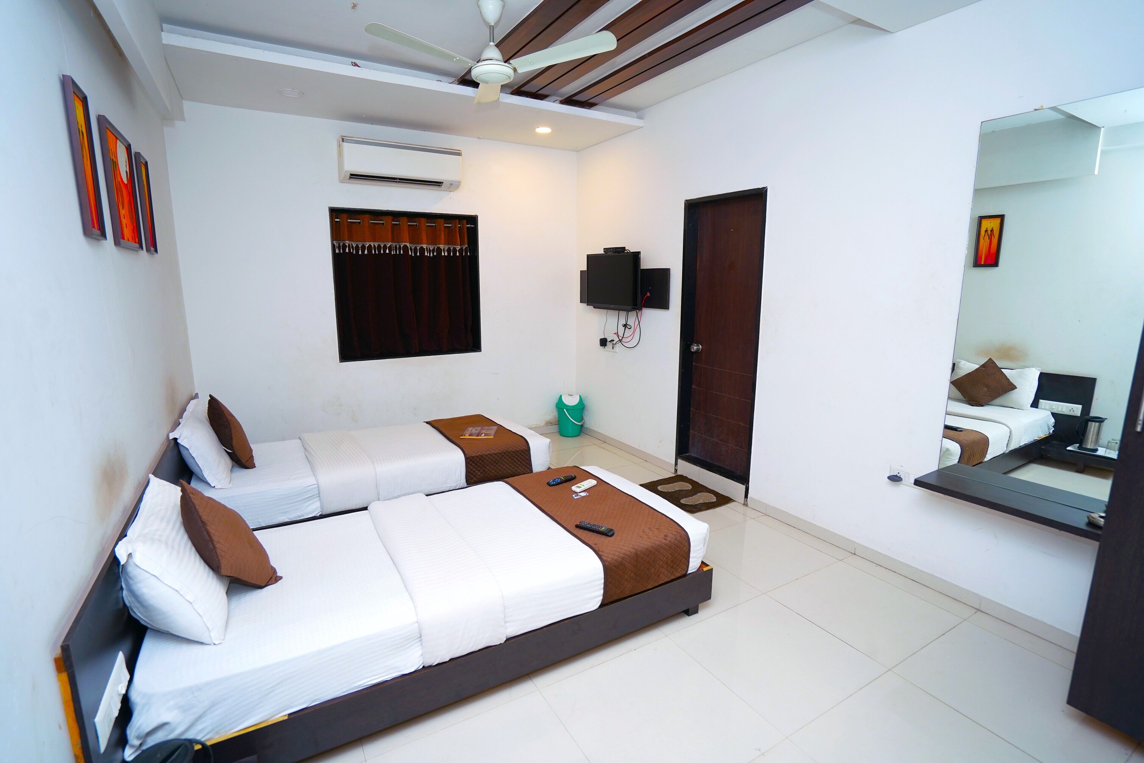 A hotel room with two beds, a ceiling fan, an air conditioning unit, a television, and a mirror.