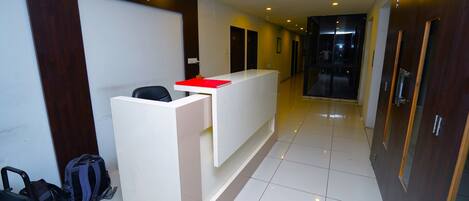A hotel reception area with a reception desk, a chair, and a backpack on the floor.