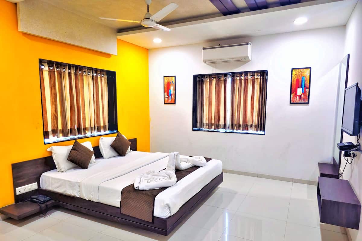 A modern hotel room with a large bed, a ceiling fan, an air conditioning unit, and artwork on the walls.