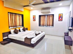 A modern hotel room with a large bed, a ceiling fan, an air conditioning unit, and artwork on the walls.
