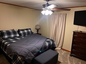 A bedroom with a bed, a ceiling fan, a dresser, and a television.