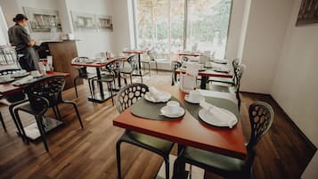 A restaurant with wooden floors, black chairs, and tables set for dining.