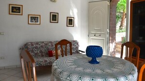 A room with a floral sofa, a round table with a crocheted tablecloth, and four framed pictures on the wall.