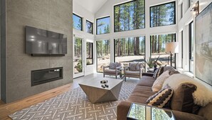 A spacious living room with a large TV, a coffee table, and a sofa with patterned cushions. - Modern Family Lodge with Access to Exclusive Golf (Bend)