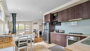 A modern kitchen with dark wooden cabinets, a stainless steel refrigerator, a gas stove, and a microwave. There is a dining area with a white table and chairs. - Rosebud Township Entertainer (Melbourne)
