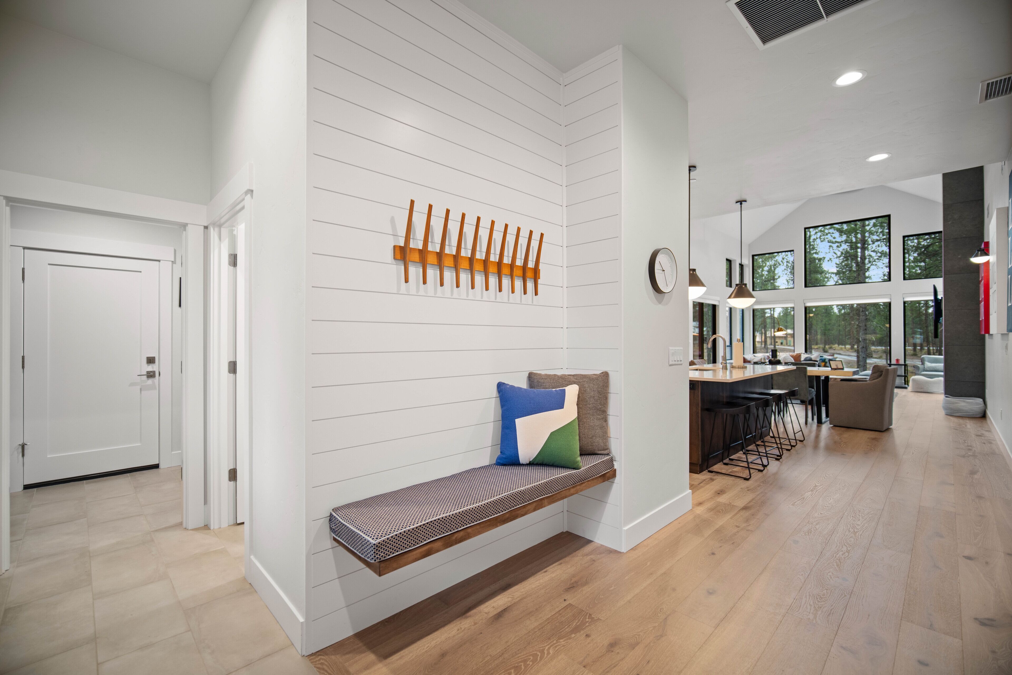 A modern interior with a bench against a white wall, a wooden slat rack, and a kitchen area with bar seating.