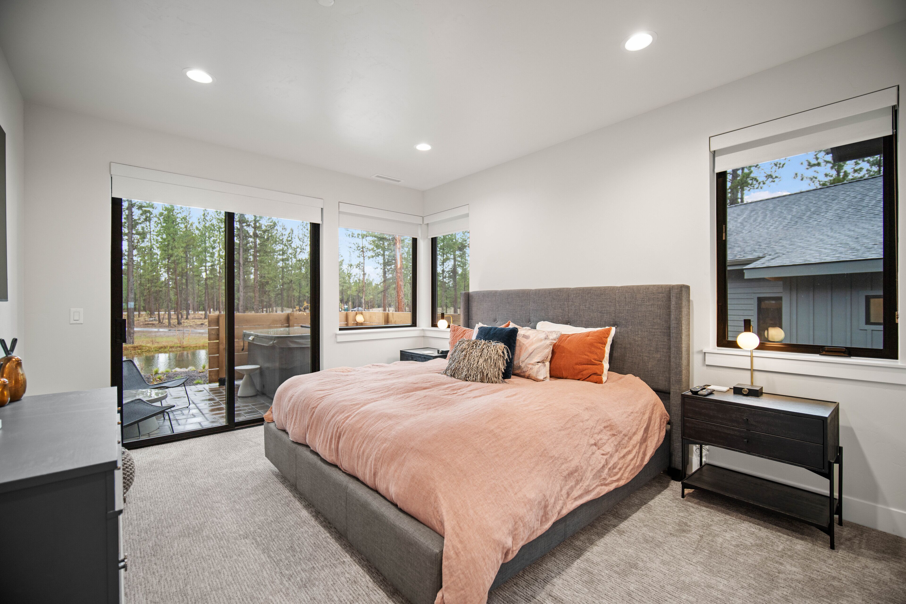 A modern bedroom with a large bed, a nightstand, and a view of the outdoors through large sliding glass doors.