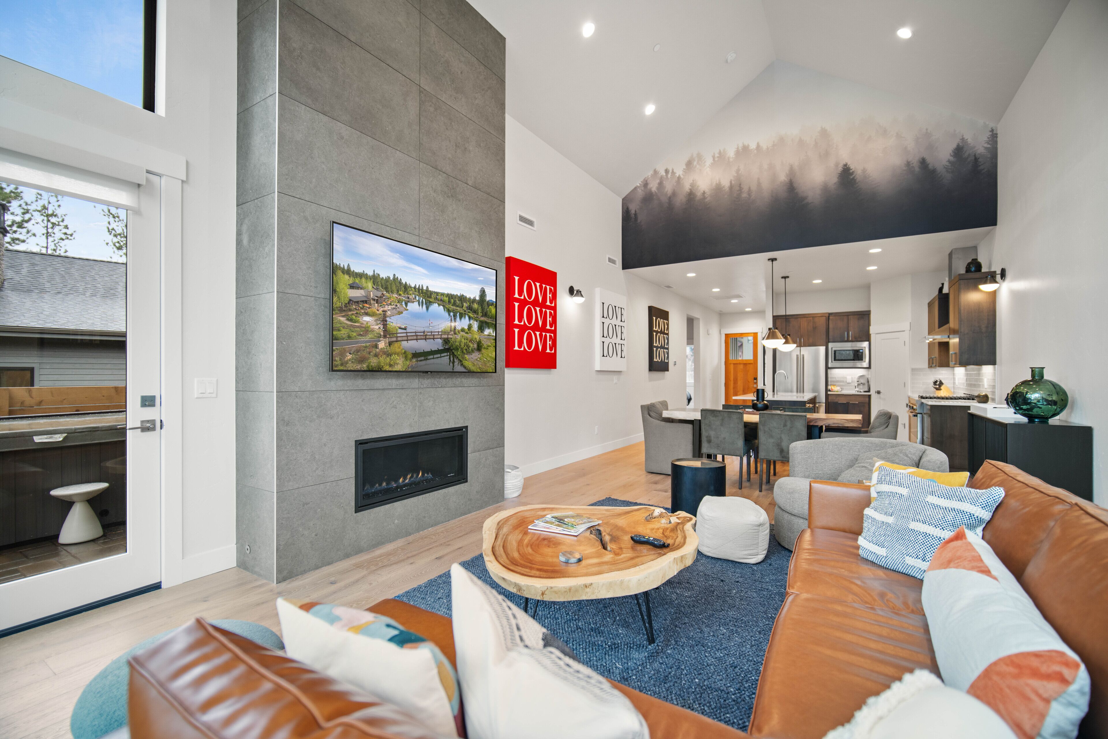 A modern living room with a fireplace, a large TV, and a dining area in the background.