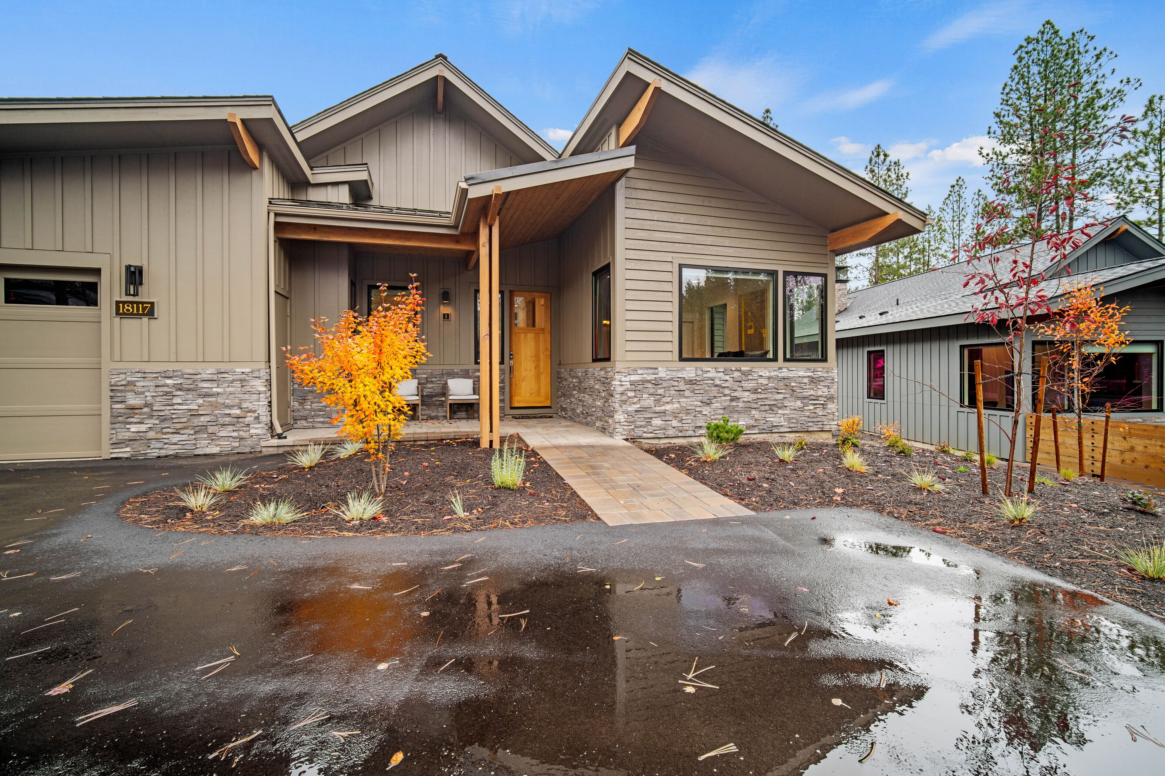 A modern two-story house with a stone foundation, a covered porch, and a well-maintained garden with autumn foliage.