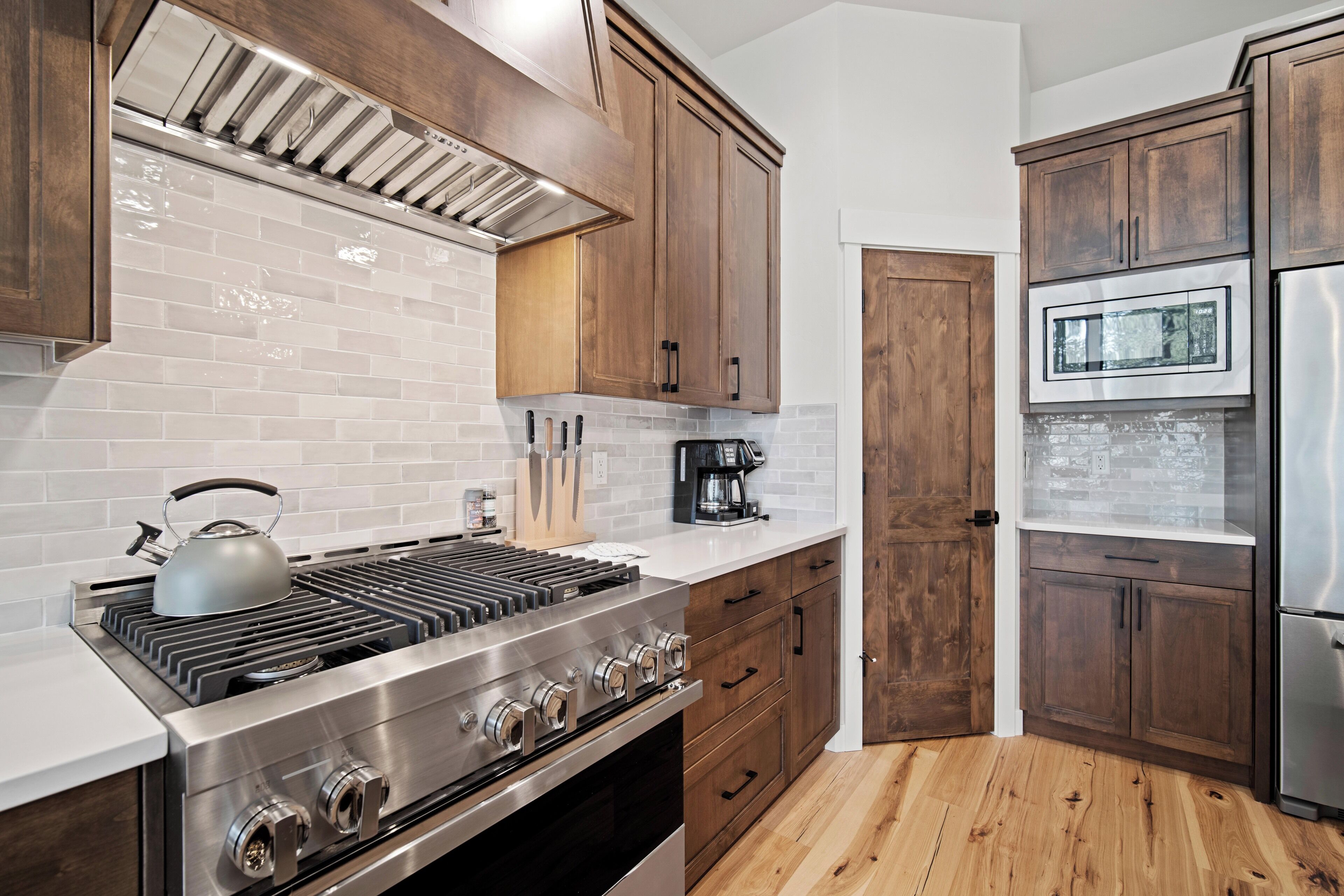 Une cuisine dotée d’une cuisinière en acier inoxydable, de meubles en bois et d’un dosseret de carrelage blanc.