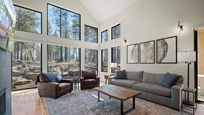 A spacious living room with large windows, a fireplace, a sofa, a coffee table, and a rug. - Caldera Couples’ Stay with Access to Exclusive Golf (Bend)