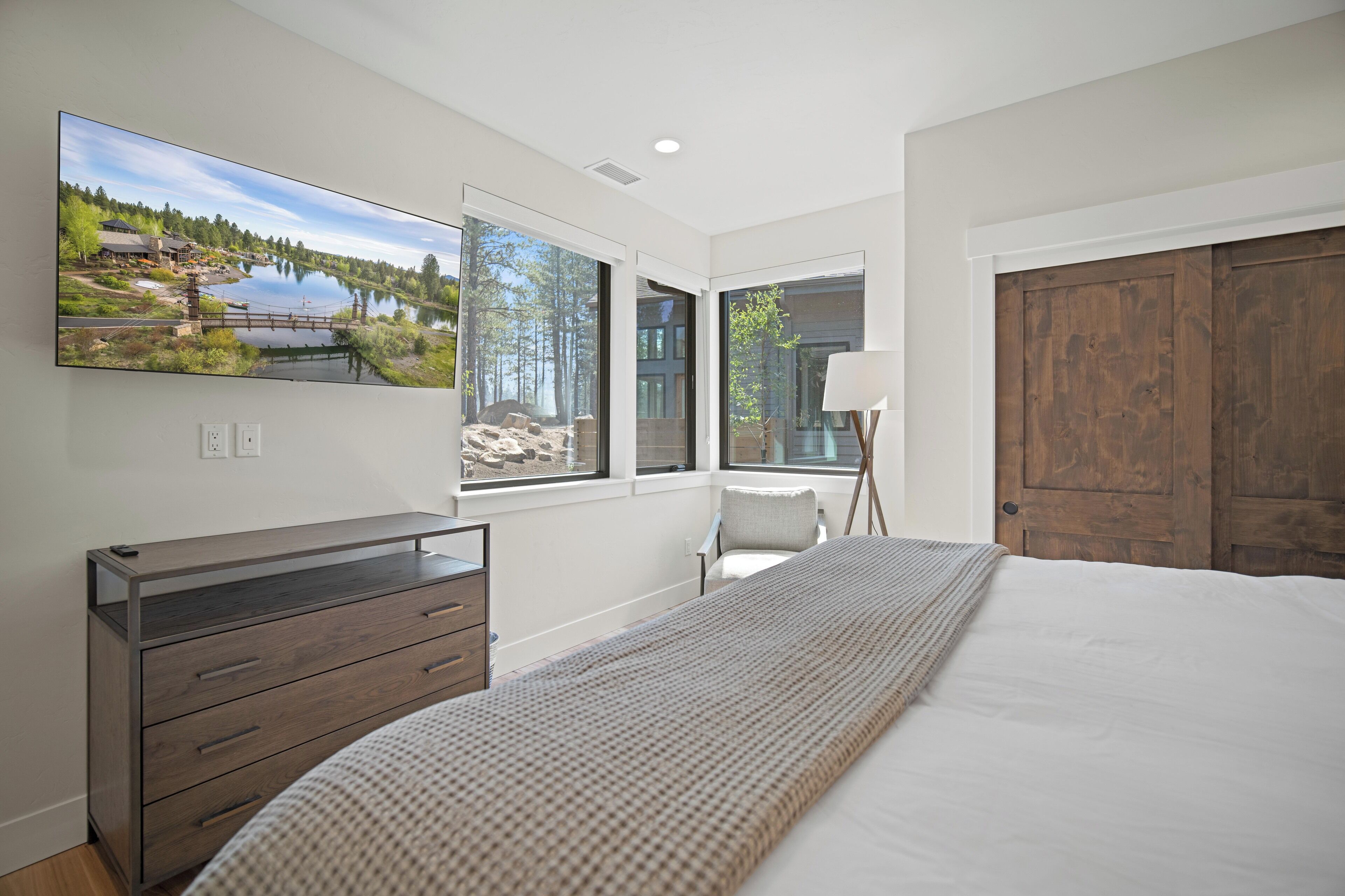 Un dormitorio con una cama grande, un aparador, una silla, una lámpara y un televisor que muestra una vista panorámica.
