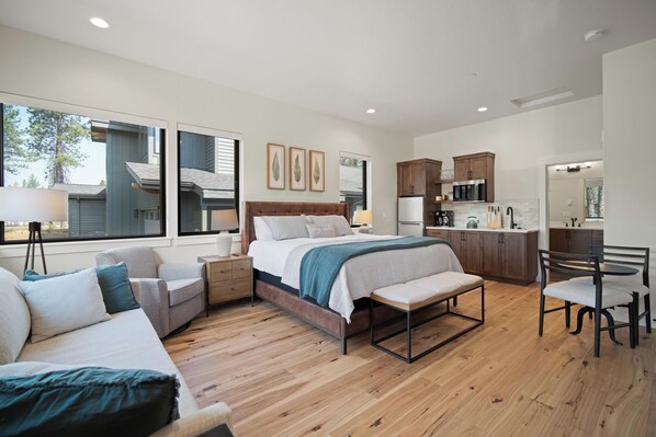 A modern bedroom with a large bed, bedside tables, a desk, and a chair. There is a view of the outside through large windows. - Forestbrook Stay with Access to Forest House (Bend)