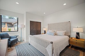 Une chambre moderne avec un grand lit, une chaise, une table de chevet et une fenêtre donnant sur une maison.