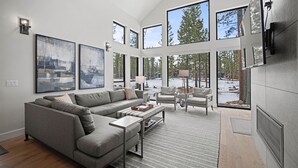 Una sala de estar moderna con un sofá modular, una mesa de centro y una chimenea. Amplias ventanas ofrecen vistas al exterior.