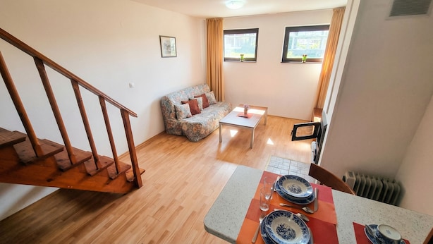 Sala de estar com sofá, mesa de centro e mesa de jantar posta com pratos e copos. Escada visível à esquerda.