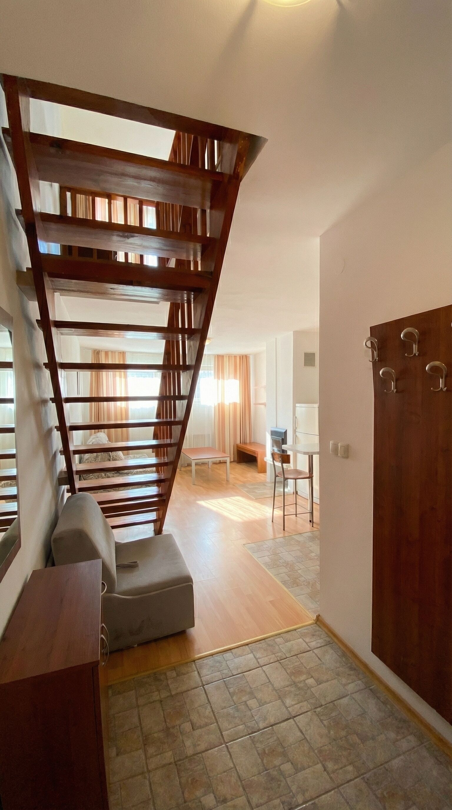 A staircase with wooden railings leading to an upper floor, a seating area with a bench and table, and a door with hooks.