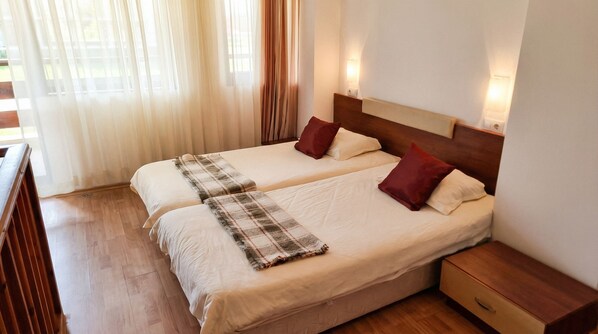 A double bed with a plaid blanket and two red pillows, wooden nightstands, and a wooden floor.