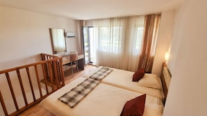 Quarto de hotel com duas camas, uma escrivaninha, um espelho e uma varanda.