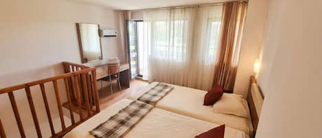 A hotel room with two beds, a desk, a mirror, and a balcony.