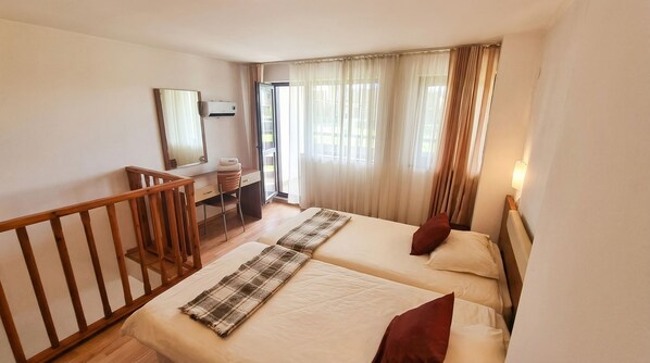 A hotel room with two beds, a desk, a mirror, and a balcony.