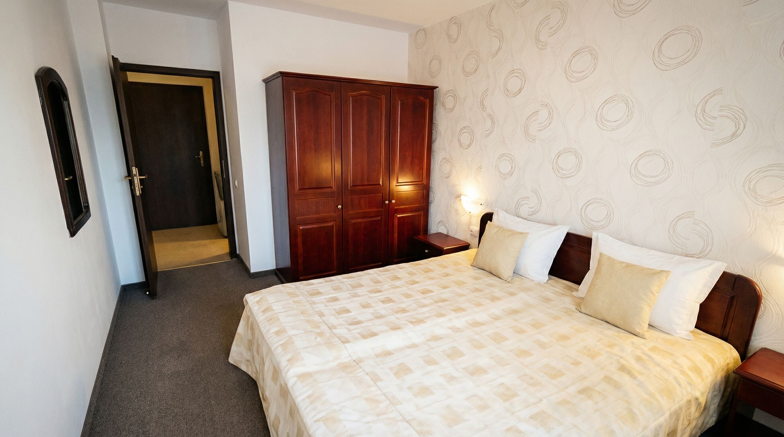 A hotel room with a bed, wardrobe, and a door leading to a hallway.