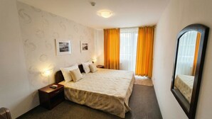 A hotel room with a bed, nightstand, wall-mounted lamp, and a large mirror. - Mountain Paradise 2 - Cosy Mountain View Apartment - 200mbps Wifi (Bansko)