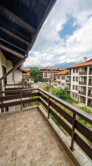 A balcony with a stone floor, wooden railing, and a view of residential buildings with red-tiled roofs.