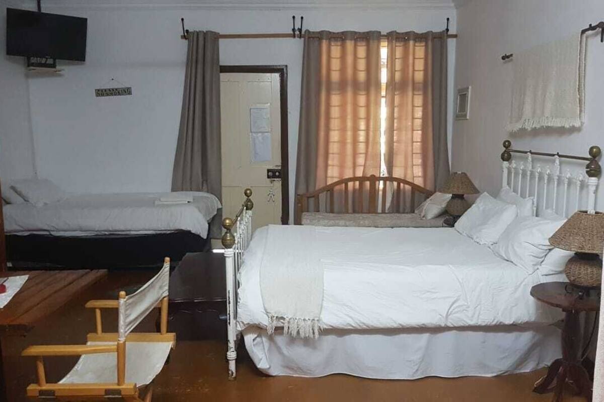A room with two single beds, a wooden table, a chair, a TV, and a window with curtains.