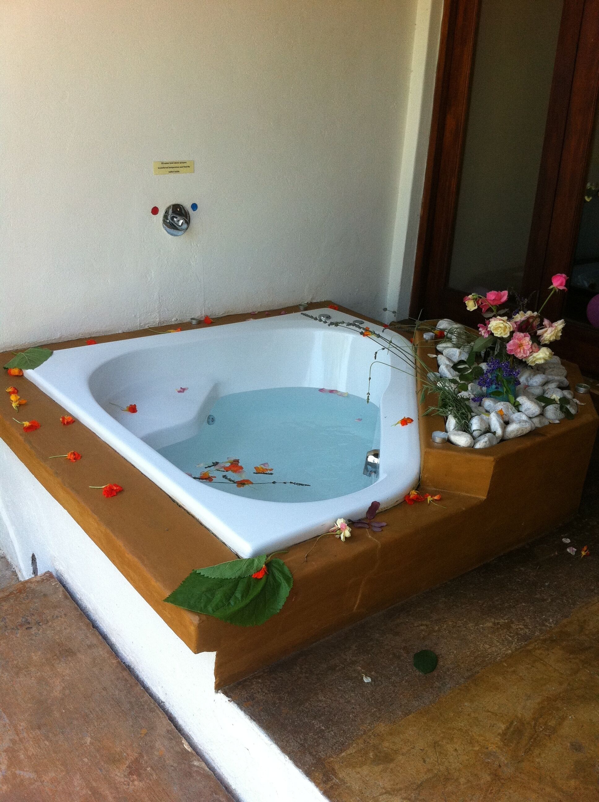 A hot tub with water, surrounded by a wooden deck and decorated with flowers and leaves.